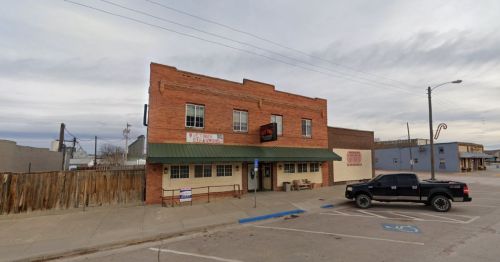 A brick building with a green awning, parked black truck, and a cloudy sky in a small town setting.