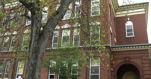 A brick building with large windows, surrounded by trees and greenery, showcasing a classic architectural style.
