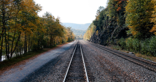 A scenic view of two parallel railway tracks surrounded by autumn foliage and mountains in the distance.