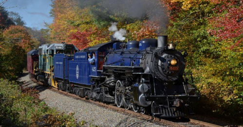 A vintage steam locomotive chugs along a scenic track surrounded by colorful autumn foliage.