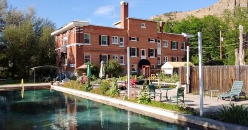 A brick building with a pool and garden, surrounded by trees and mountains on a sunny day.