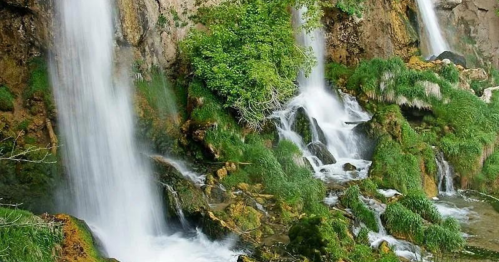 A serene landscape featuring cascading waterfalls surrounded by lush greenery and rocky terrain.