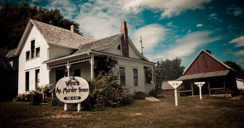 The Villisca Axe Murder House, a historic white house with a sign, surrounded by green grass and blue skies.