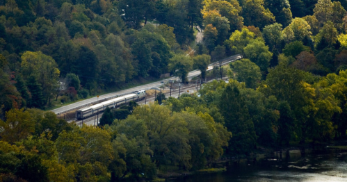 Aerial view of a train traveling through lush green trees alongside a river.