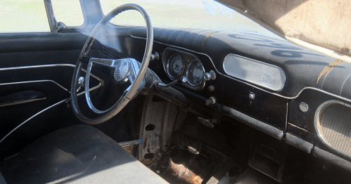 Interior of an old car with a worn steering wheel, dashboard, and seats, showing signs of age and neglect.