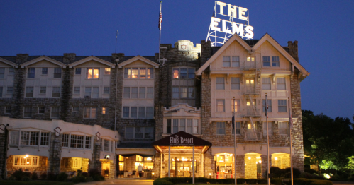 The Elms Resort building at night, featuring a lit sign and stone architecture.