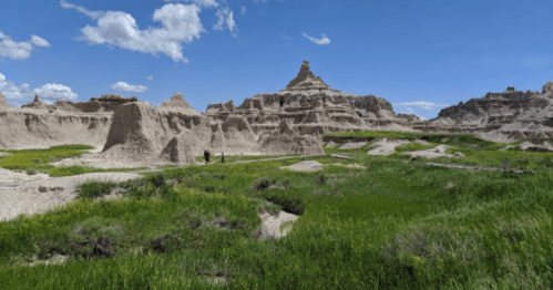 A scenic view of rugged rock formations and green grass under a bright blue sky with scattered clouds.