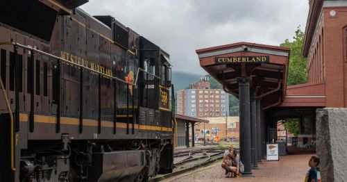 A vintage train at Cumberland station, with children exploring nearby under a cloudy sky.