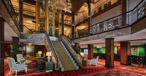 Elegant hotel lobby featuring a grand staircase, ornate chandeliers, and stylish seating areas with rich decor.