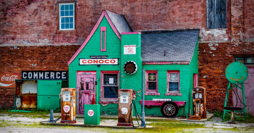 Colorful vintage gas station with a green and pink building, old gas pumps, and a brick wall backdrop.