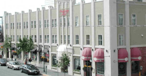 A multi-story building with a light green facade, featuring red awnings and parked cars in front.