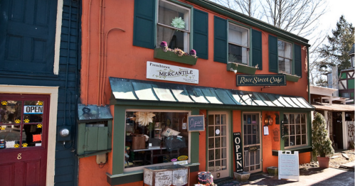 A colorful storefront featuring "Pennhaven Mercantile" and "Rose Street Café," with an open sign and decorative plants.