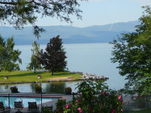 A serene lake view with mountains in the background, surrounded by trees and colorful flowers in the foreground.