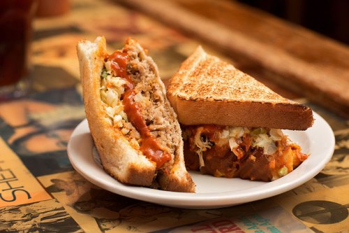 A plate with two toasted sandwiches filled with meat, sauce, and coleslaw, resting on a table with a vintage design.