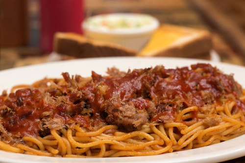 A plate of spaghetti topped with pulled meat and marinara sauce, served with a side of coleslaw and toast.