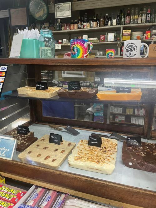 Display case filled with various fudge flavors, labeled with signs, in a cozy shop setting.