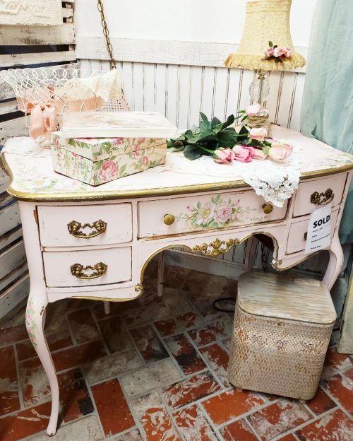 Vintage pink dresser with floral design, gold accents, and decorative items, set in a charming interior space.