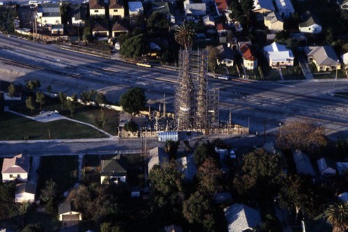Aerial view of a construction site surrounded by residential houses and a road, with scaffolding visible.