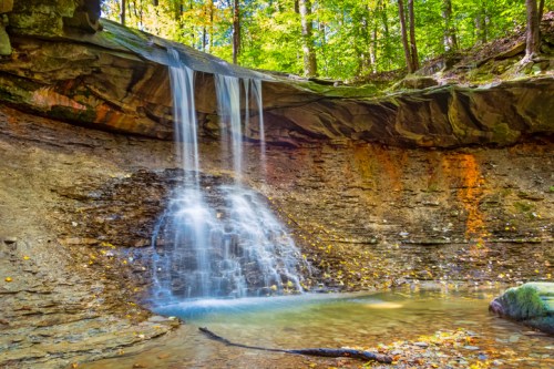 A serene waterfall cascades over rocky cliffs into a tranquil pool, surrounded by vibrant autumn foliage.