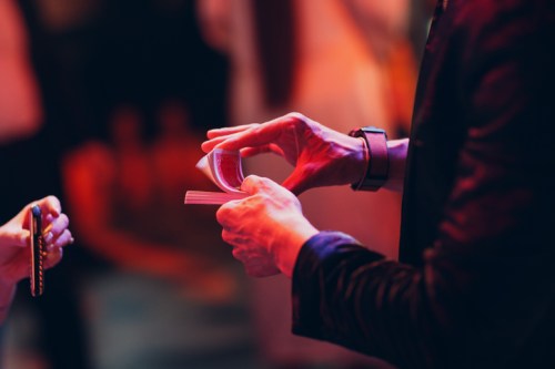 A person holding a deck of cards, preparing to perform a card trick, with a blurred audience in the background.