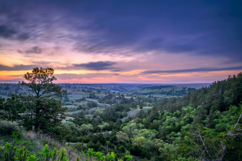 A scenic view of rolling hills and lush greenery under a colorful sunset sky.