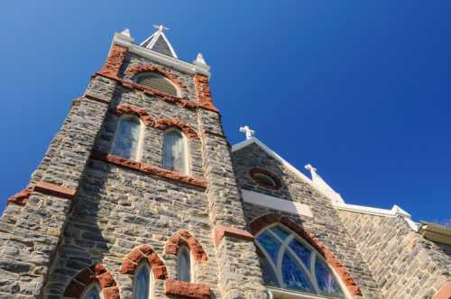 A tall stone church tower with a cross, featuring arched windows against a clear blue sky.