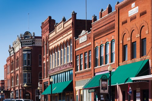Historic brick buildings with green awnings line a sunny street, showcasing vintage architecture and storefronts.
