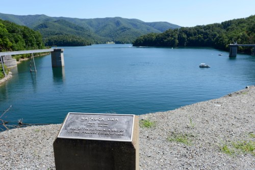 View of a serene lake with mountains in the background, featuring a plaque about Watauga Dam in the foreground.