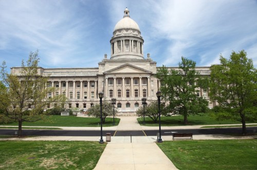A grand government building with a dome, surrounded by green trees and a clear blue sky.