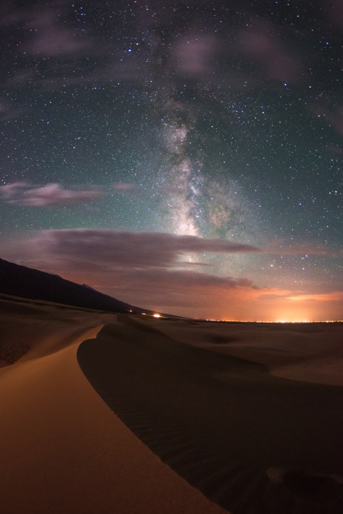 A stunning night sky filled with stars and the Milky Way over a desert landscape, with gentle sand dunes in the foreground.