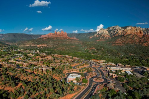 Aerial view of Sedona, Arizona, showcasing red rock formations, green trees, and a roundabout in the foreground.