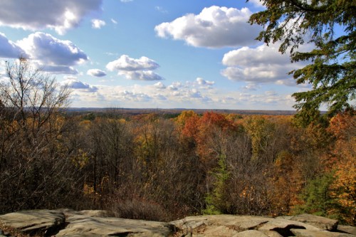 A scenic view of a colorful autumn landscape with trees and clouds under a blue sky.