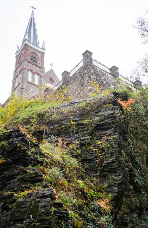 A stone church tower rises above a rocky hillside, adorned with autumn foliage and a misty sky.