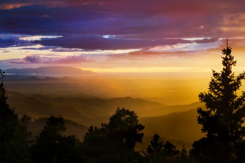 A stunning sunset over a mountainous landscape, with vibrant colors and silhouettes of trees in the foreground.