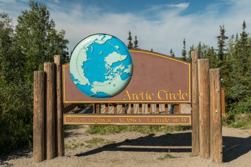 Sign marking the Arctic Circle on the Dalton Highway in Alaska, featuring a globe illustration and latitude details.