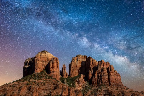 A stunning night sky filled with stars above majestic red rock formations, showcasing the Milky Way in the background.