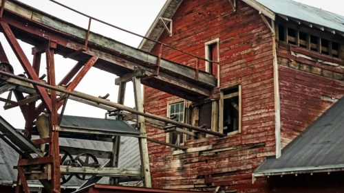 A weathered red barn with a wooden conveyor system, featuring broken windows and a rustic, industrial appearance.