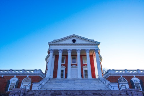 A grand building with columns and a clock, set against a clear blue sky, viewed from the bottom of a staircase.
