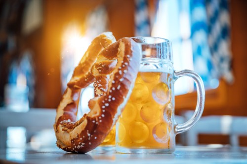 A frosty mug of beer next to a large, salted pretzel, with warm sunlight streaming in through a window.