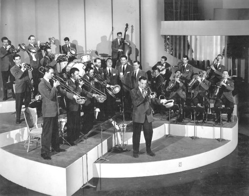 A large jazz band performs on stage, featuring musicians with various instruments in a vintage setting.