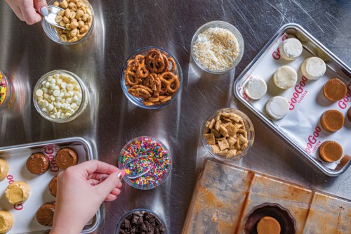 A variety of toppings and treats, including nuts, pretzels, and sprinkles, arranged on a table for dessert preparation.