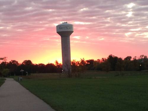 A water tower silhouetted against a vibrant sunset, with a path and trees in the foreground.