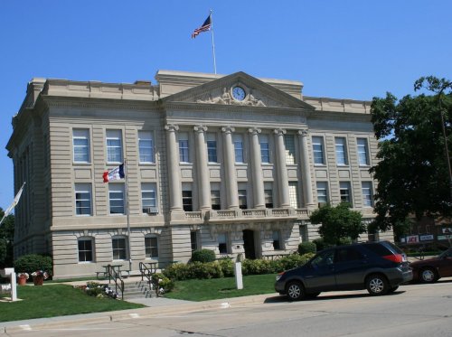 Historic courthouse with columns, a clock, and flags, set against a clear blue sky and green landscaping.