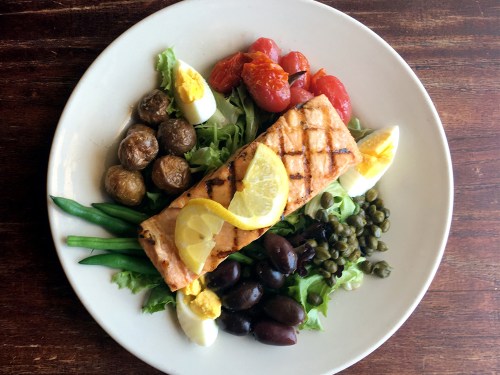 Grilled salmon with lemon, served on a bed of greens with olives, capers, cherry tomatoes, and boiled eggs.