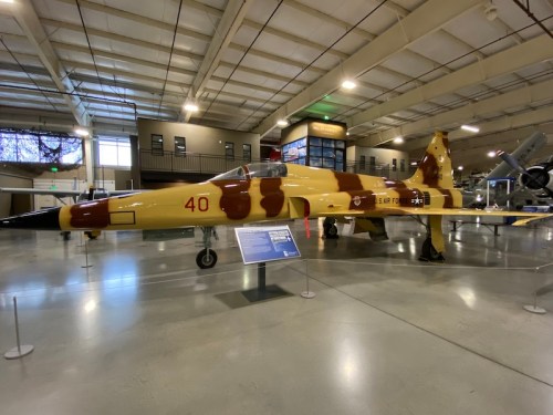 A military jet displayed in a museum, featuring a yellow and brown camouflage pattern.