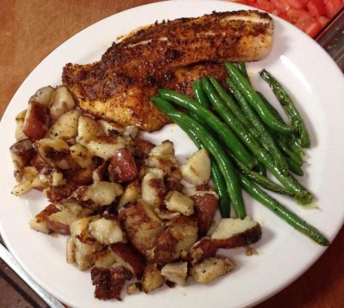 A plate with seasoned fish fillet, roasted red potatoes, and green beans.