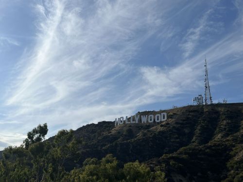 The iconic Hollywood sign on a hillside, surrounded by trees and a blue sky with wispy clouds.