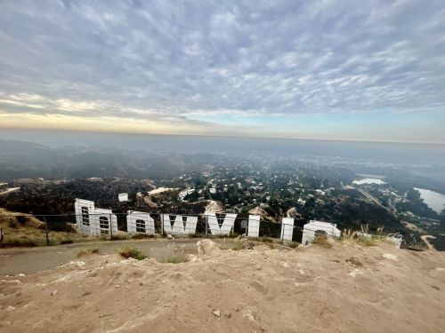 View of the Hollywood sign from a distance, surrounded by hills and a cloudy sky.