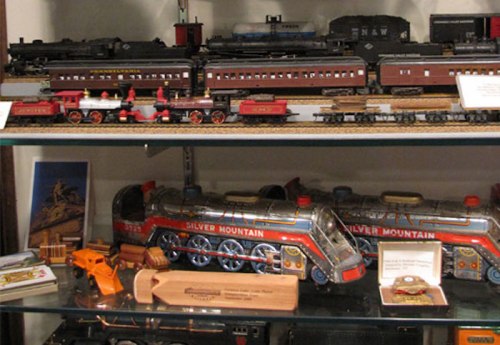 A display of model trains and toy train sets on shelves, featuring various styles and colors.