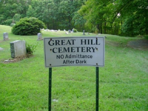 Sign for Great Hill Cemetery, stating "No Admittance After Dark," surrounded by green grass and trees.